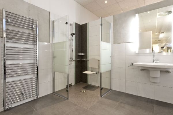 Barrierefreies Bad mit ebener Dusche, Duschsitz, Handtuchheizkörper und wandhängendem Waschbecken.