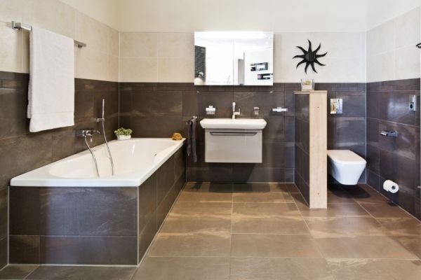 Helles Bad mit Wanne, Waschbecken, Spiegel und separater WC-Nische, Fliesen in Beige und Dunkelbraun.